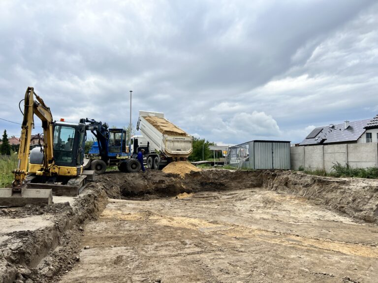 Wykop fundamentowy na placu budowy z koparką i wywrotką, ilustrujący wpływ rodzaju gruntu na koszty budowy domu